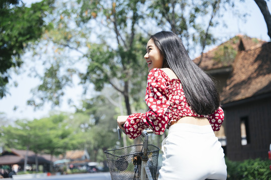 在传统村庄骑自行车的穿红衬衫的黑色长发妇女的背照。