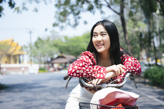 穿红衫的黑色长发女孩在村里停下来骑自行车时，双手托在自行车上。