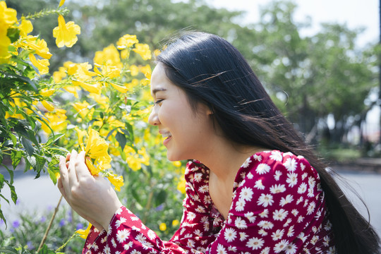 在阳光明媚的日子里，穿着红衬衫的黑色长发女孩抚摸着黄花。