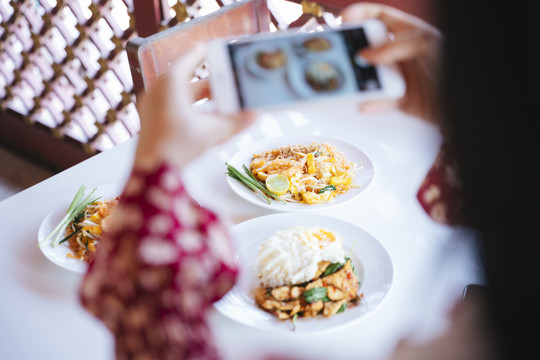 穿着红衬衫的女人用智能手机拍下餐厅桌上食物的照片时，智能手机的图像被剪短了。