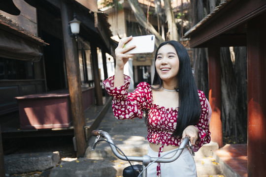 穿红衫的黑长发女孩在当地传统村落的集市上骑着自行车散步并拍照留念。