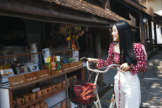 穿红衫的黑长发女孩在当地传统村落的集市上骑着自行车散步并拍照留念。