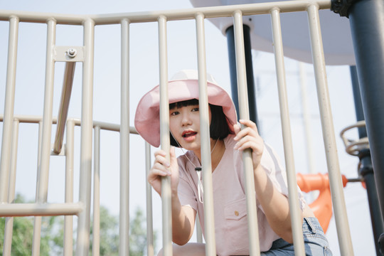 美丽的亚洲女人戴着帽子在操场上玩耍，坐在笼子后面。