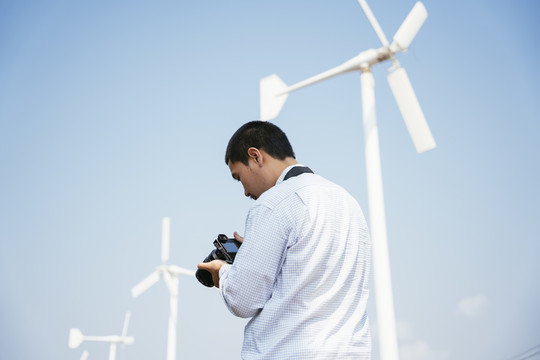 光头摄影师用相机拍摄风车的后景。