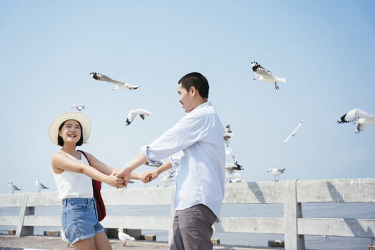 亚泰夫妇喜欢牵着对方的手，在海边的桥上观光，看一群围着他们飞行的海鸥。自然界的野生动物。