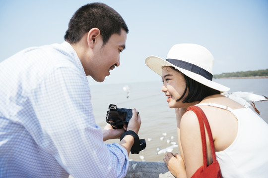 快乐的亚泰夫妇在海边用相机互相展示照片。在海上大桥上旅行。