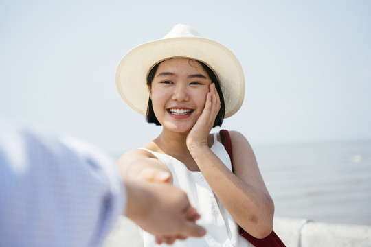 特写-快乐的泰国亚裔女子戴着帽子牵着男友的手在海桥上。