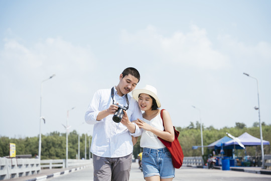 亚泰夫妇走在海边大桥上看镜头。一对幸福的旅游情侣在相机里看照片。