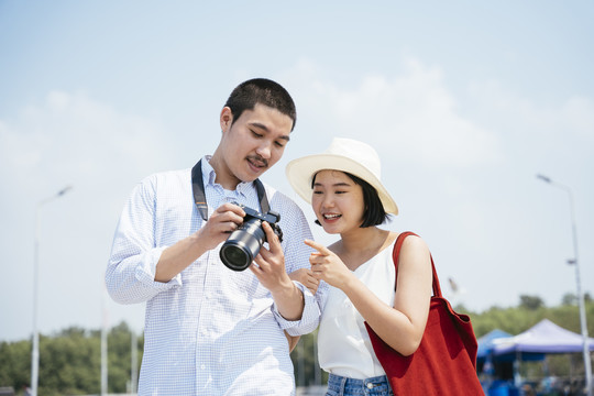 亚泰夫妇走在海边大桥上看镜头。一对幸福的旅游情侣在相机里看照片。