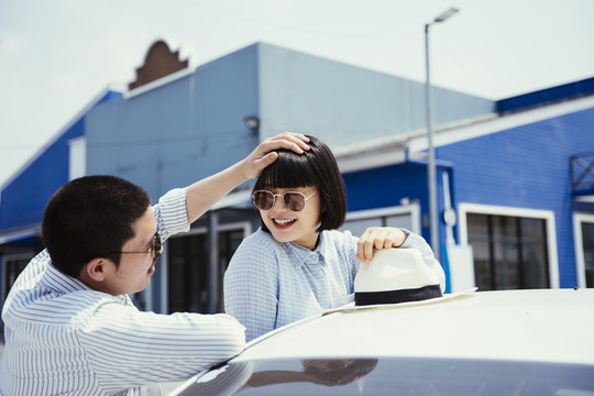 一对戴着墨镜的浪漫亚泰情侣在车外对视。男人摸女人的头。