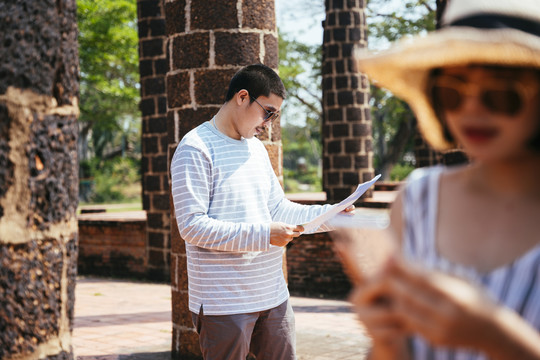 光头游客戴着墨镜在古城遗址看纸质地图。