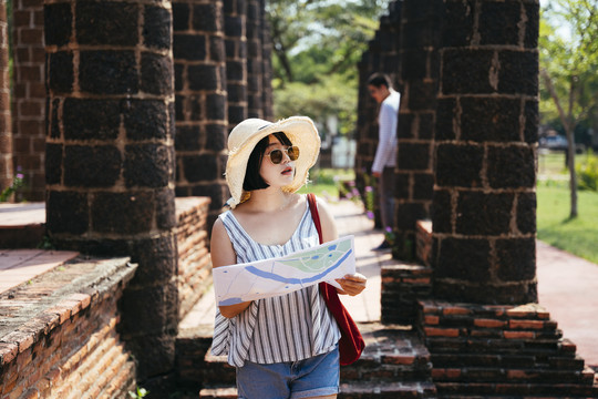 戴着帽子和太阳镜的亚泰游客手持一张古城遗址纸质地图。