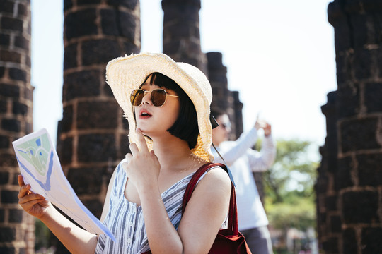 戴着帽子和太阳镜的亚泰游客手持一张古城遗址纸质地图。
