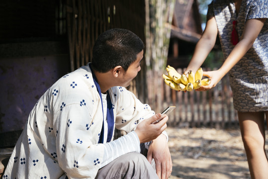 生态旅游-美丽的亚洲女人给坐在地板上的男人香蕉。巴南提议。