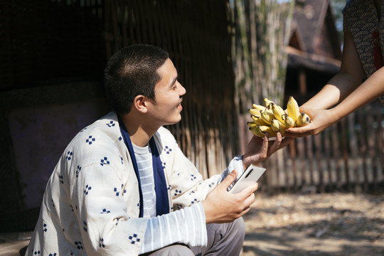 生态旅游-快乐男人从女孩手中接过巴南。女孩向游客提供香蕉。