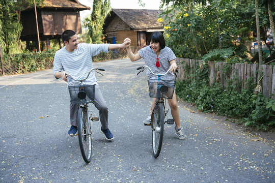 生态旅游-亚洲旅游情侣手牵手一起骑自行车。
