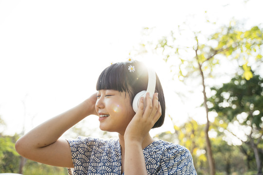 亚洲女人鲍勃发型闭上眼睛听音乐用白色耳机在户外的自然公园。