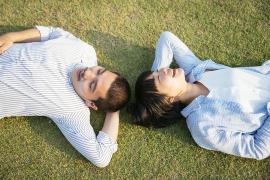 顶视图-亚泰夫妇头对头躺在户外的草地上。在大自然中放松。