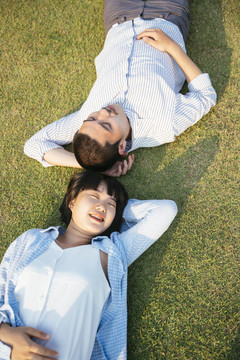 顶视图-亚泰夫妇头对头躺在户外的草地上。在大自然中放松。