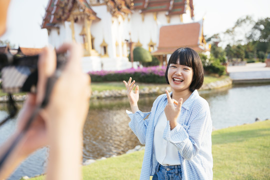 亚洲男朋友在河边的佛寺用相机给女友拍照。