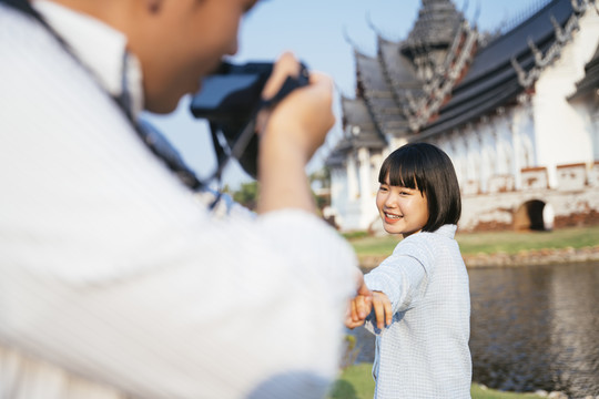 亚洲男朋友在河边的佛寺用相机给女友拍照。