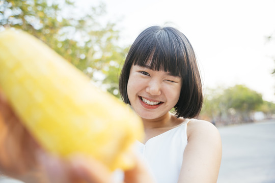 特写亚洲女人鲍勃发型吃煮玉米户外。健康的水果和蔬菜。