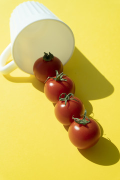 草莓和西红柿从黄色背景的白色杯子里溢出。