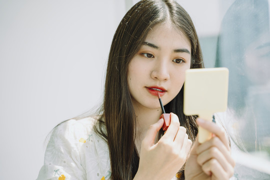美丽的亚洲年轻的泰国妇女做化妆前使用唇膏在镜子前。