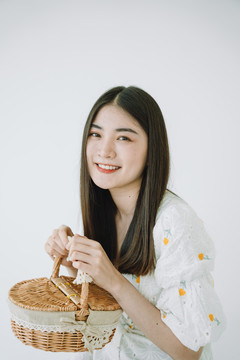 美丽的亚洲年轻泰国女子长长的黑发和稻草野餐篮。隔离在白色背景上。