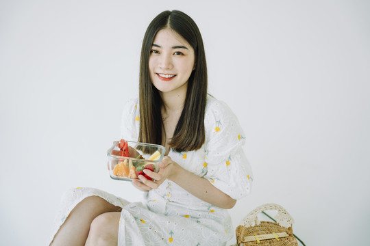 美丽的亚洲年轻泰国女子长发，深色的水果放在玻璃碗里。野餐的概念。隔离白色背景。