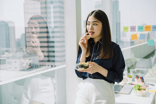 美丽的亚泰长黑发女子在办公室公寓房间享用健康食品春卷。