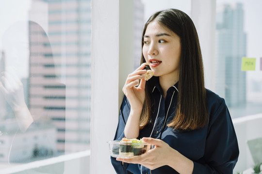 美丽的亚泰长黑发女子在办公室公寓房间享用健康食品春卷。