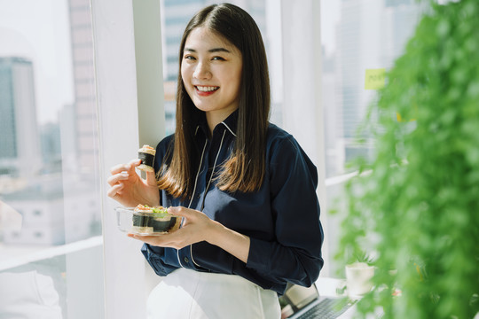 美丽的亚泰长黑发女子在办公室公寓房间享用健康食品春卷。