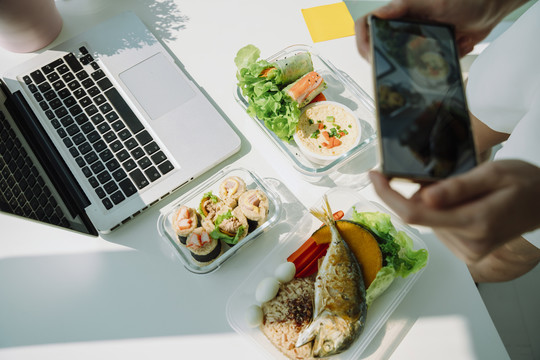 女性手持智能手机在办公桌上拍摄健康食品的俯视图。复制空间。