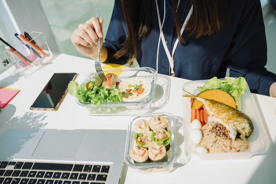 商务女性在办公室餐桌上吃健康食品的俯视图。沙拉蝴蝶结。春卷。泰国菜。智能手机旁边的饭菜。