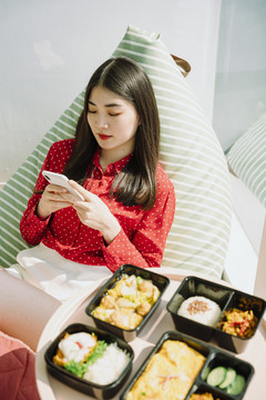 美丽的亚泰黑发红衫女子在吃饭前使用智能手机。