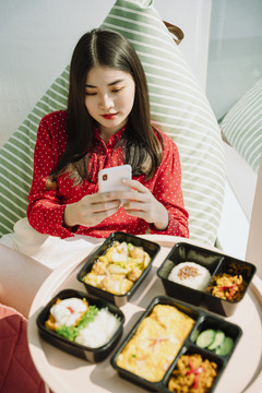 美丽的亚泰黑发红衫女子用智能手机拍摄美食美酒。先吃饭。