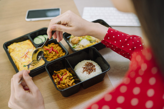 亚泰妇女在餐桌上吃泰国食物午餐盒的俯视图。