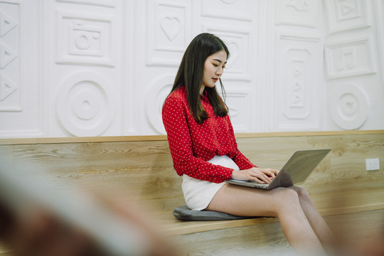 美丽的亚泰长黑发红衫女子在家里用笔记本电脑工作。在家工作。在家工作。