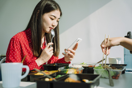 穿着红衫的泰国亚裔美女一边吃一边看电话。坏习惯。