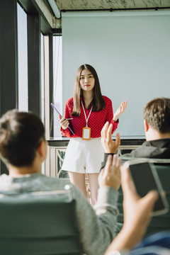 在会议室里，身着红衫的美丽的年轻亚泰女商人在人们面前做报告。人们举手向她提问。