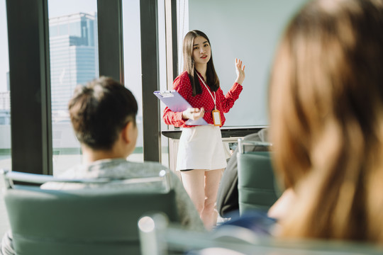 在会议室里，身着红衫的美丽的年轻亚泰女商人在人们面前做报告。人们举手向她提问。