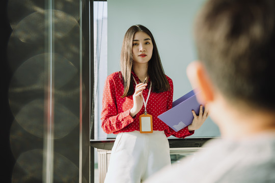 在会议室里，身着红衫的美丽的年轻亚泰女商人在人们面前做报告。人们举手向她提问。