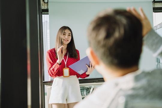 在会议室里，身着红衫的美丽的年轻亚泰女商人在人们面前做报告。人们举手向她提问。