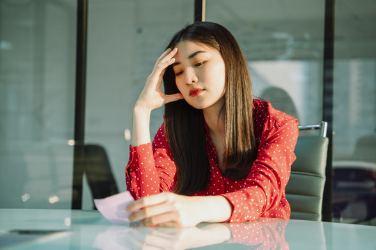 美丽的年轻亚泰女商人在红衫阅读粘不张贴它的关切和担心的表情。