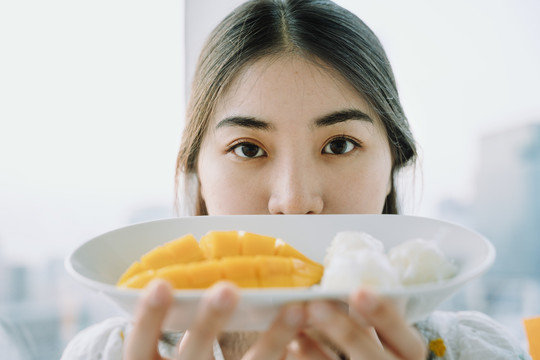 一个快乐的亚泰女人拿着一盘芒果糯米的特写镜头。商业用途。泰国甜点。