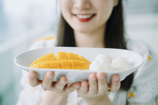 一个快乐的亚泰女人拿着一盘芒果糯米的特写镜头。商业用途。泰国甜点。
