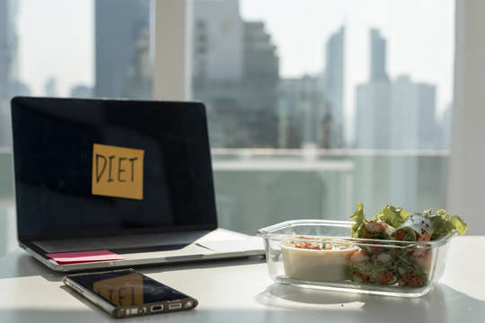 城市背景。办公桌配有笔记本电脑和新鲜春卷。健康饮食。
