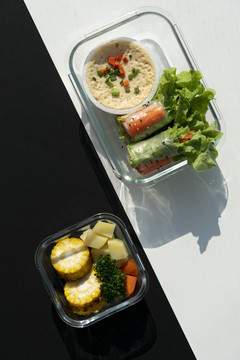 面包卷和烤蔬菜的俯视图在黑白图案背景上的玻璃容器中。