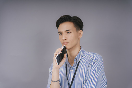 身着蓝领衬衫的泰国帅哥自信地拿着智能手机。商业用途。